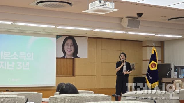 Yong Hye-in speaking at a podium with a screen behind her displaying 'Basic Income's past 3 years' and her name.